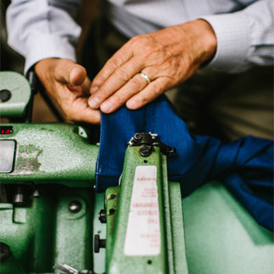 Close-up of a person’s hands guiding blue fabric through a green industrial sewing machine.