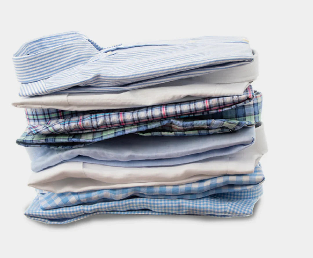 A stack of neatly folded mens shirts in various patterns and shades of blue, including stripes, checks, and plaid, on a white surface.