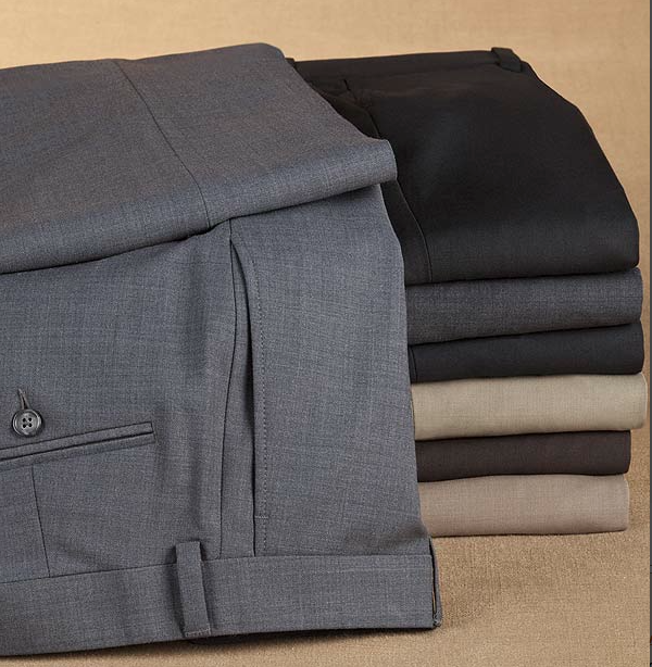 A stack of neatly folded dress pants in various colors, including grey, black, beige, and brown, placed on a tan surface.