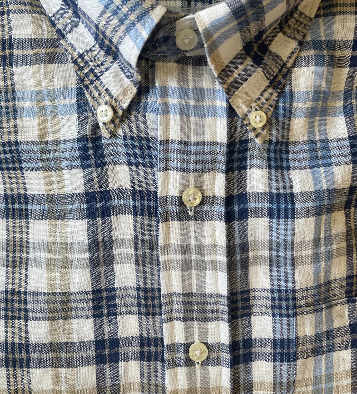 Close-up of a collared shirt with a blue, beige, and white plaid pattern and white buttons.