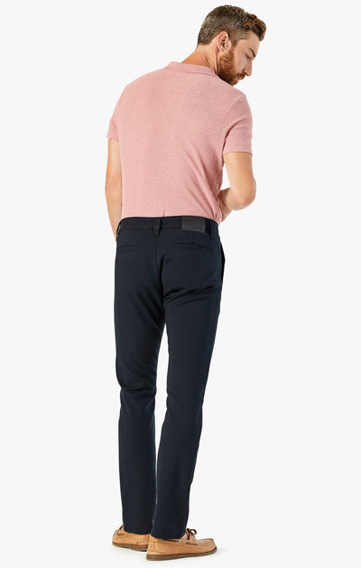 A man stands facing away, wearing a pink short-sleeve polo, tan loafers, and 34 Heritage Black High-Flyer slim trousers by 34 Heritage against a plain white background.
