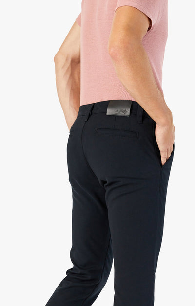 Seen from the back against a white background, a person with hands in pockets wears a light pink short-sleeve shirt and 34 Heritage Black High-Flyer chinos by 34 Heritage.