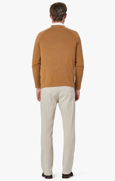 A man faces away, wearing 34 Heritage Dawn Twill straight-leg pants in light beige by 34 Heritage, paired with a brown sweater and dark shoes, set against a plain white background.