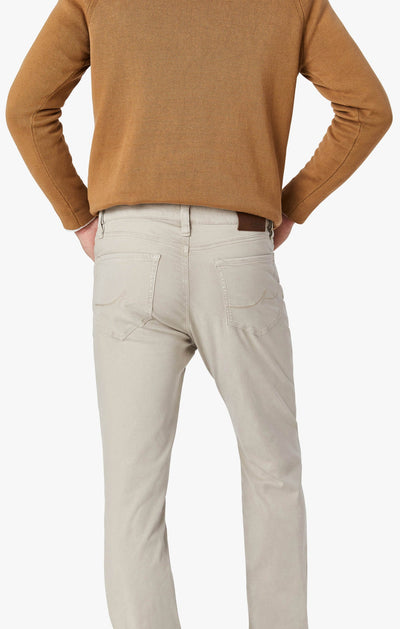 A person is shown from the back, wearing a brown long-sleeve shirt with 34 Heritage Dawn Twill light beige straight leg pants, hands on hips against a white background.
