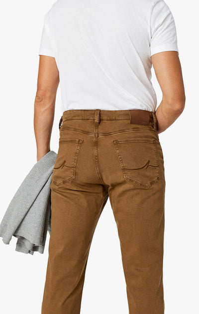 Someone is shown from the back wearing 34 Heritage Tobacco Twill straight leg pants and a white T-shirt, holding a gray sweater in their left hand.
