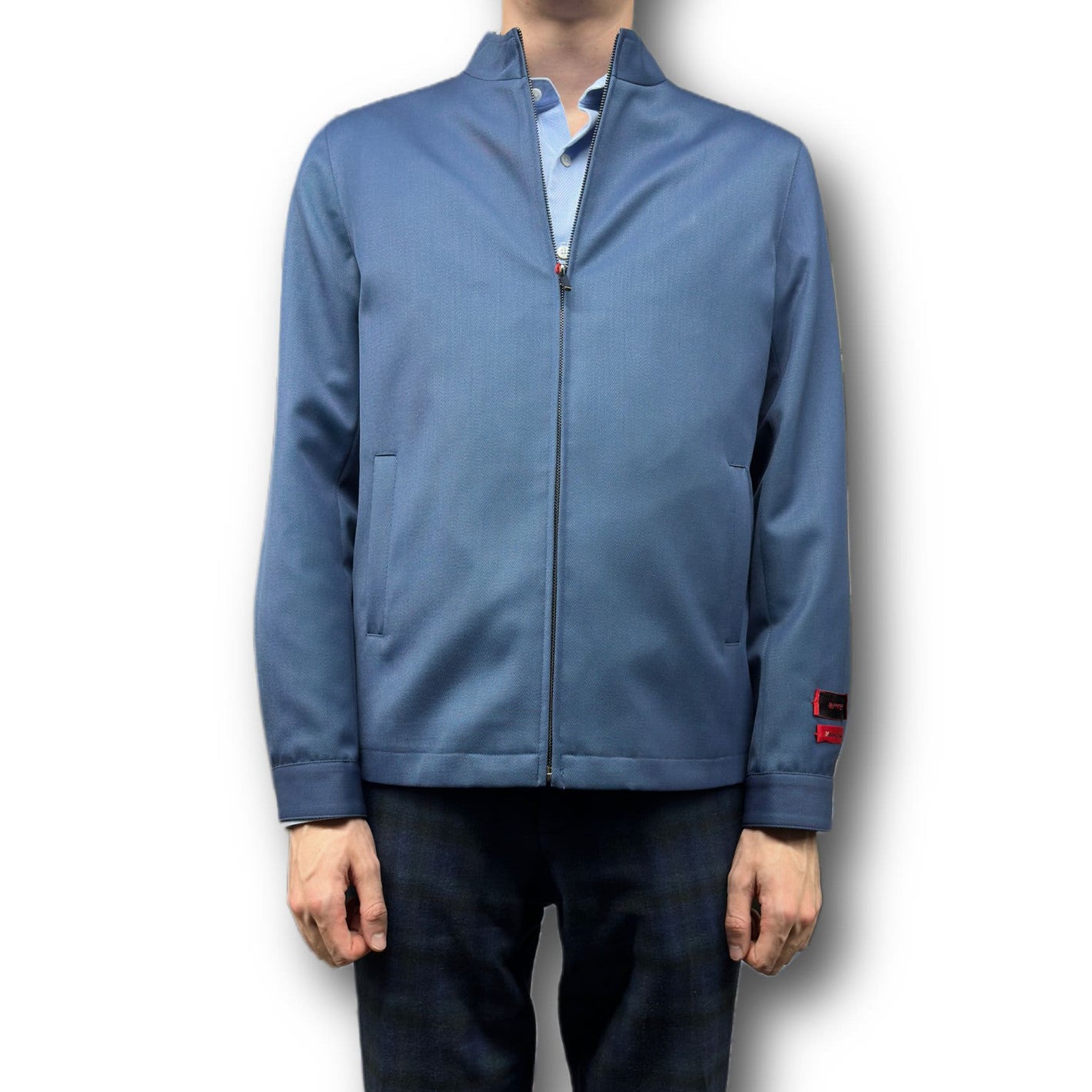 A person in a blue zip-up jacket, light blue shirt, and dark plaid pants stands against a white background, showcasing refined style similar to the Mattarazi Coat Paolo by Mattarazi.