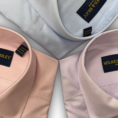 Three Wilkes & Riley Twill Stripe Dress Shirts in light blue, pink, and lavender are neatly folded and arranged in a triangular pattern on a white background.