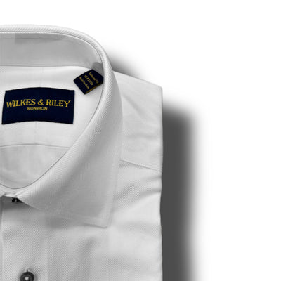 A folded white Wilkes & Riley Herringbone Dress Shirt Big & Tall with a “WILKES & RILEY NON IRON” label inside the collar is displayed on a white background, highlighting its wrinkle-free, non-iron comfort and style.