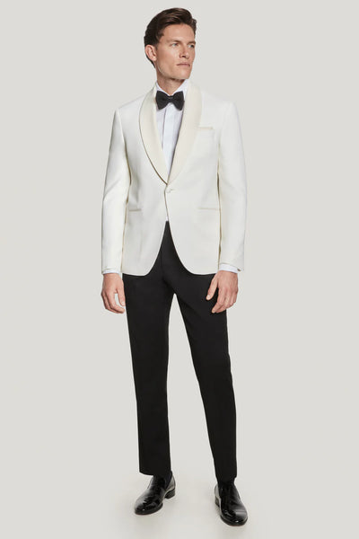 A man wears the Jack Victor Ethan Cream Dinner Jacket with a matching shawl collar, a white dress shirt, black bow tie, Super 120's wool black dress pants, and black dress shoes, standing against a plain background.