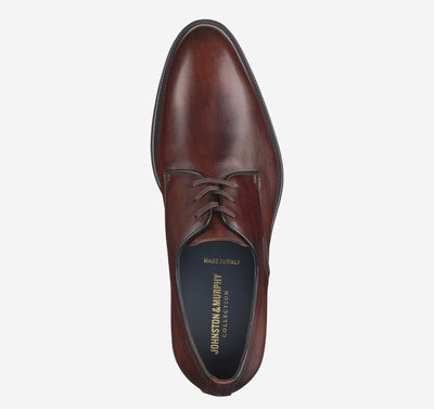 A single Johnston & Murphy Flynch Plain brown leather dress shoe with laces is shown from above, featuring Italian hand-stained uppers, a dark sole, branded insole, and soft leather linings for comfort.
