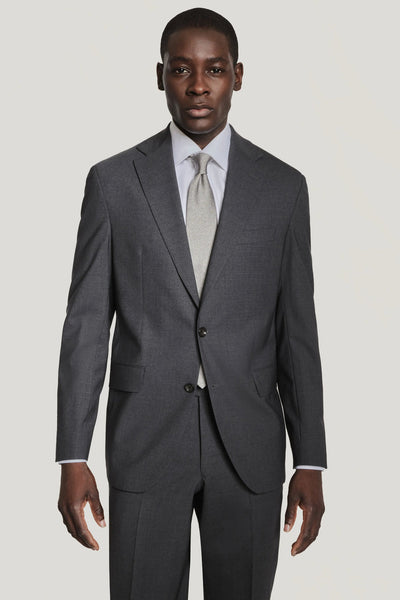A man stands facing forward against a plain light background, wearing the Jack Victor Solid Wool Suit in dark gray with a light gray tie and white dress shirt.