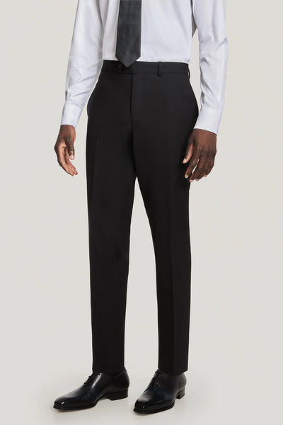 A man wearing a Jack Victor Solid Wool Suit from Jack Victor, paired with a wrinkle-resistant white dress shirt, dark tie, and black dress shoes, standing with his arms at his sides.