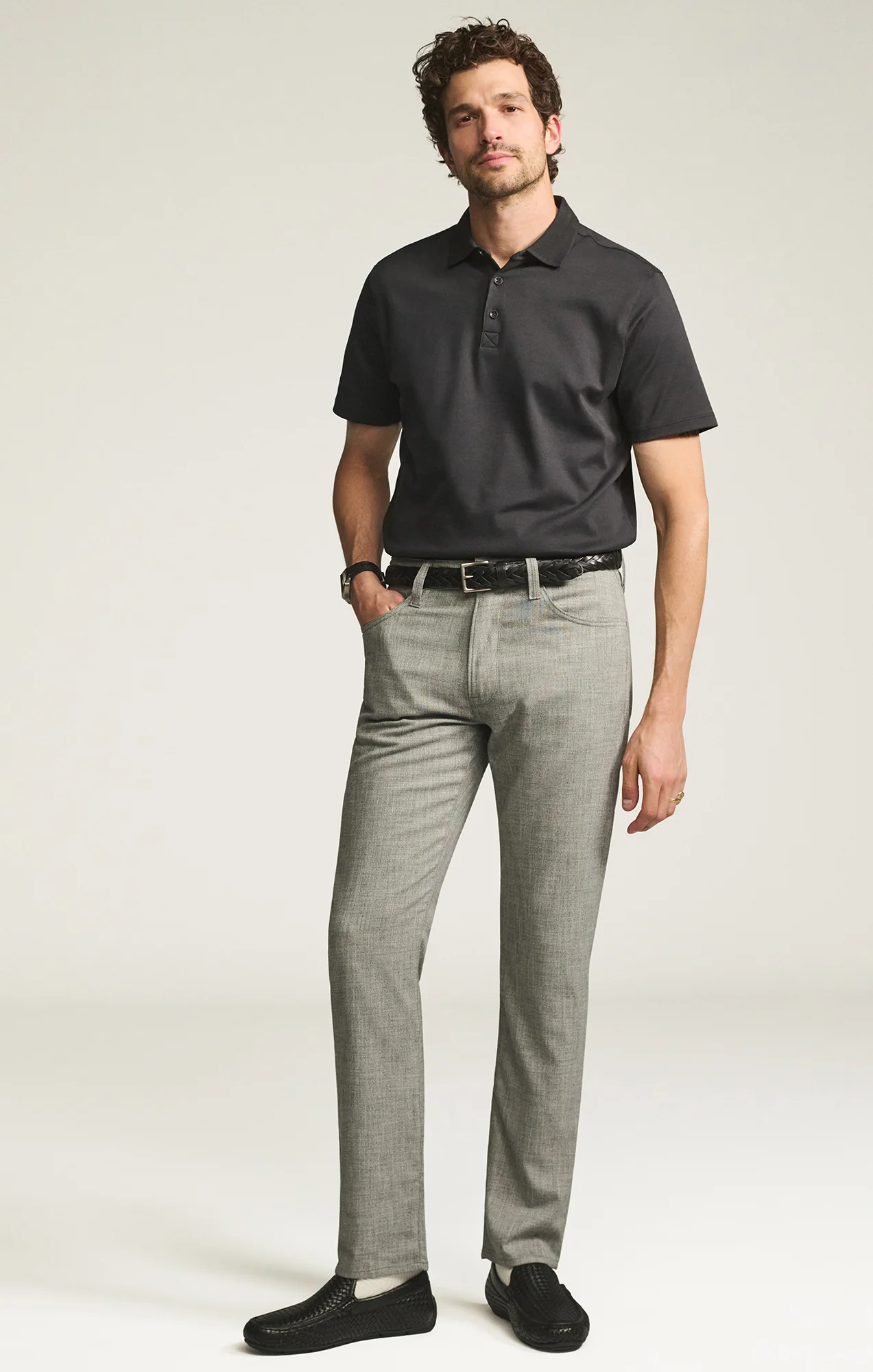 Man wearing a black polo shirt and gray pants on a white background