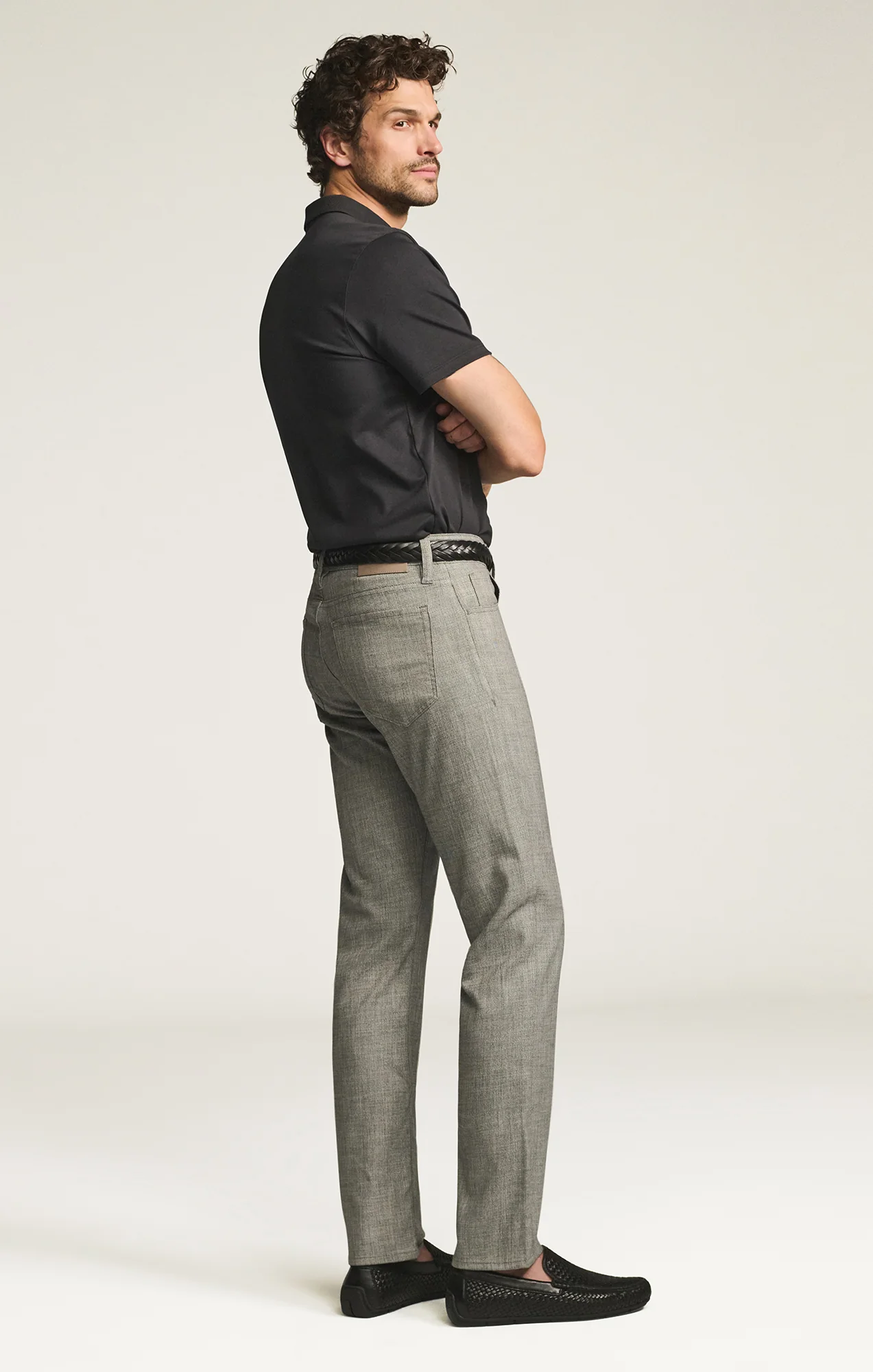 Man wearing a black polo shirt and gray pants on a white background