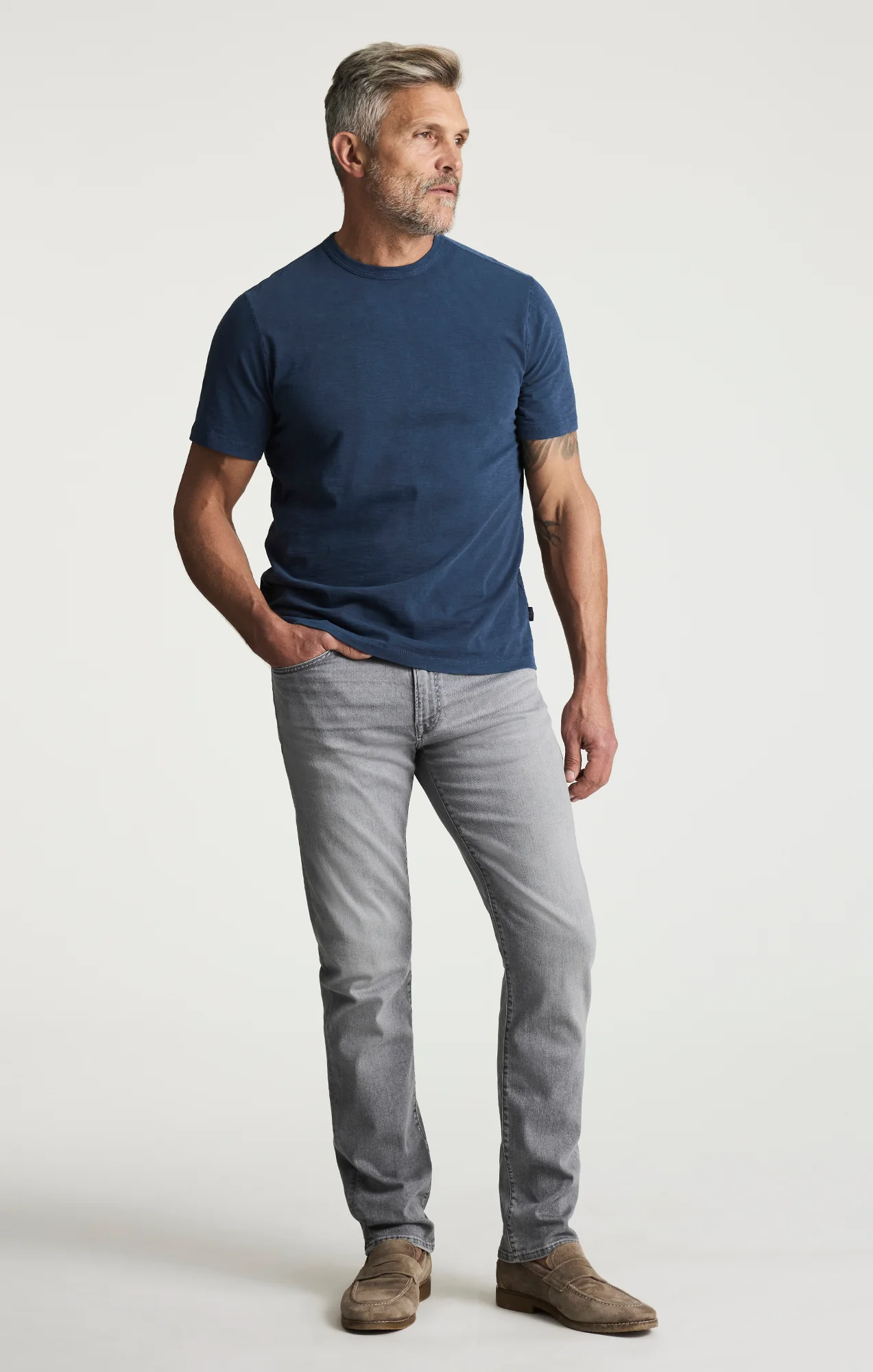Man wearing a navy blue t-shirt and gray jeans on a white background