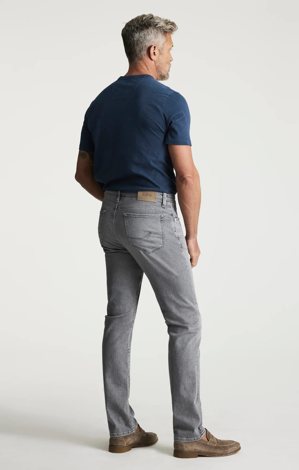 Man wearing a navy blue t-shirt and gray jeans on a white background