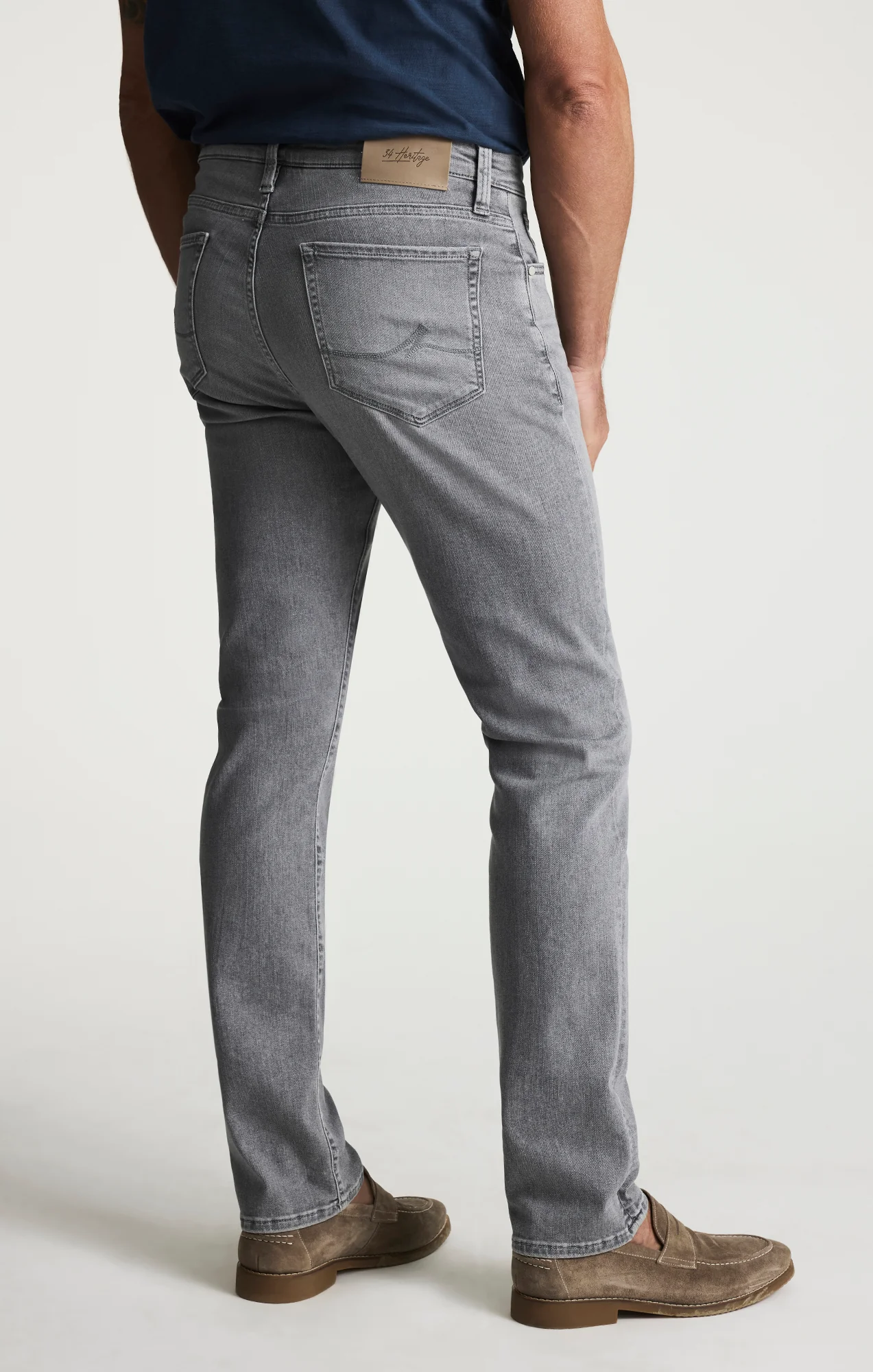 Person wearing gray jeans and brown shoes on a white background