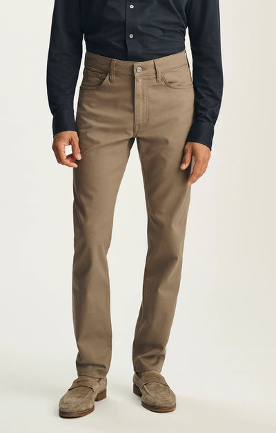 A person wearing a dark button-down shirt, 34 Heritage Courage Coolmax straight-leg khaki dress pants, and grey suede loafers.