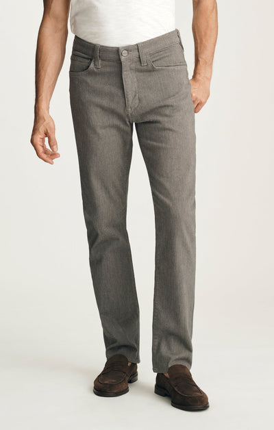 A person wearing the 34 Heritage Charisma Diagonal Big&Tall relaxed straight leg trousers in gray, a white T-shirt, and brown loafers stands against a plain background.