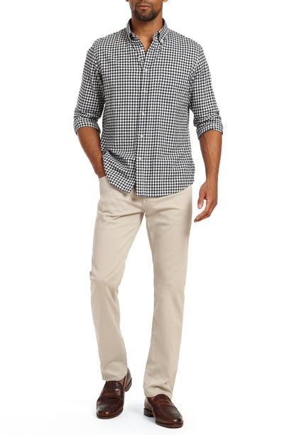 Man wearing 34 Heritage Charisma Coolmax Big & Tall Jeans by 34 Heritage, paired with a black and white checkered shirt and brown loafers, standing with one hand in his pocket.