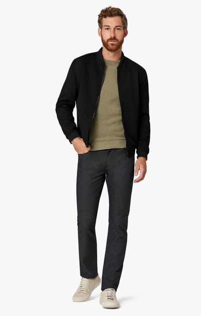 Man wearing a black jacket, green shirt, and dark pants on a white background