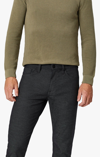 Person wearing a green textured sweater and dark pants on a white background