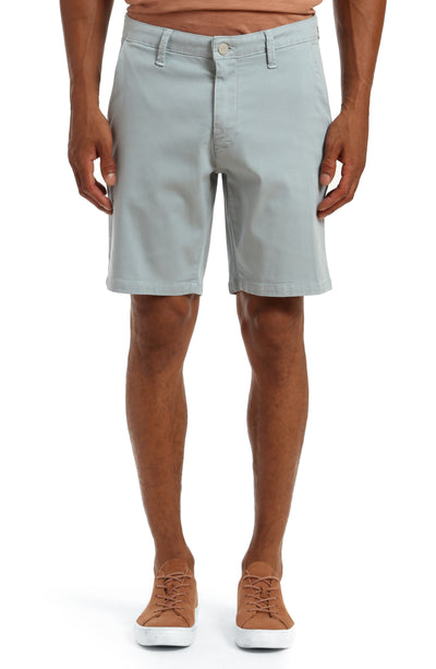 A person stands against a white background wearing 34 Heritage Nevada Soft Touch Shorts in light gray, paired with a brown shirt and brown sneakers.