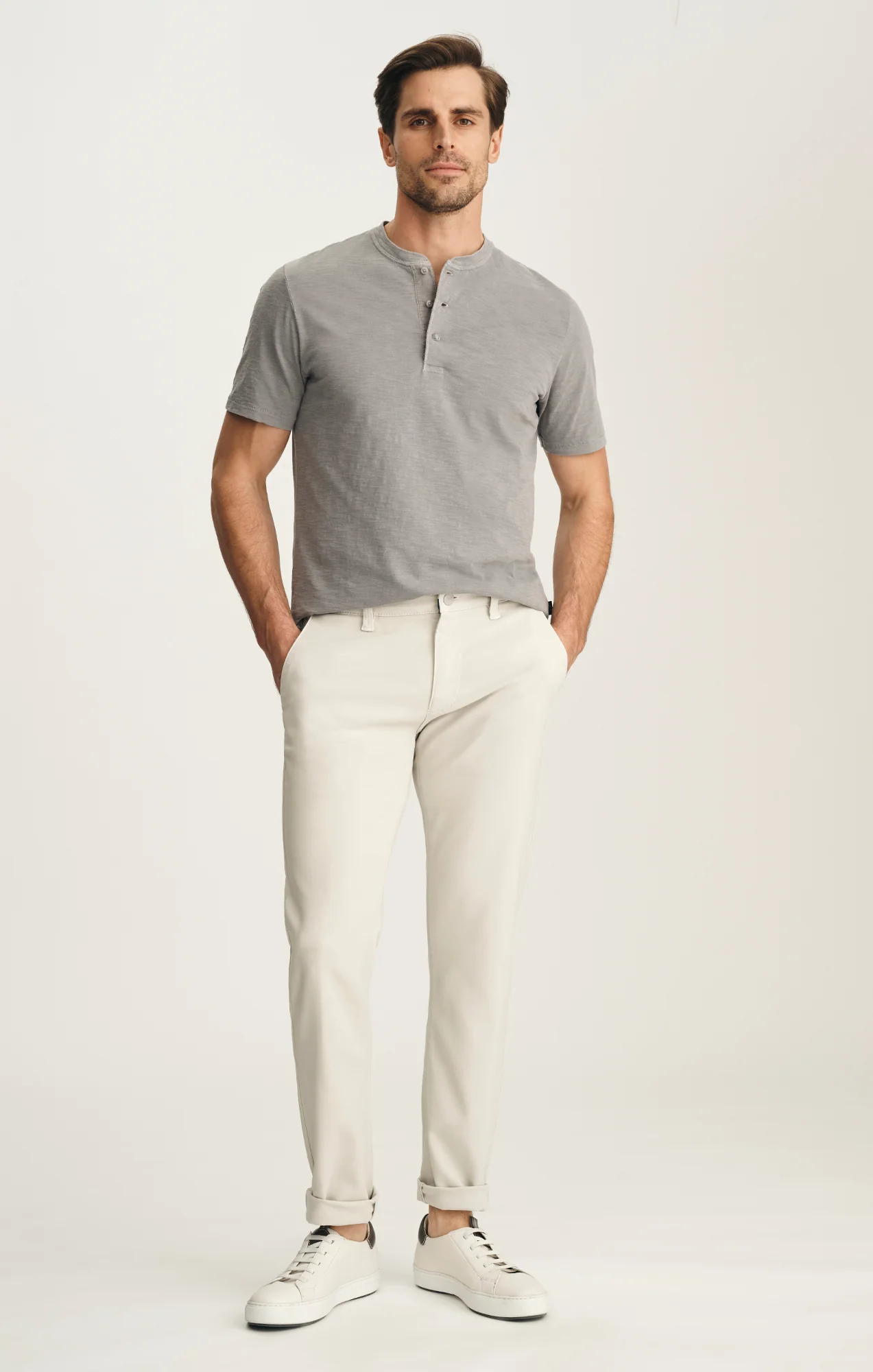 Man wearing a gray henley shirt and white pants on a light background