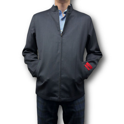 A man wears the Mattarazi Coat Paolo, a dark grey zip-up bomber by Mattarazi with a stand collar and red sleeve tab, layered over a light blue shirt and paired with dark jeans.