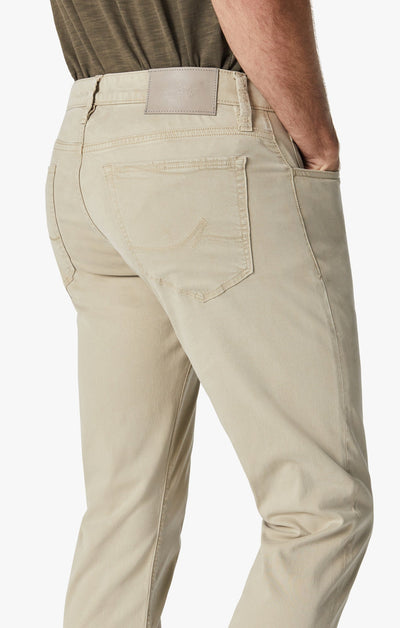 Model wears 34 Heritage Aluminum Twill jeans in a relaxed straight-leg fit, beige color, by 34 Heritage, shown from the back with one hand in a pocket and paired with a brown shirt.