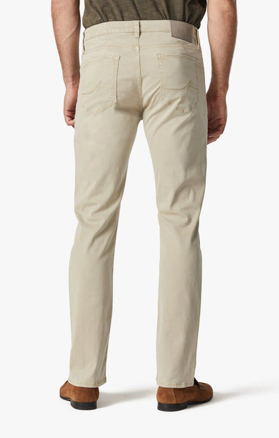 A person, seen from the back, wears 34 Heritage Aluminum Twill light beige jeans in a relaxed straight-leg fit with brown shoes, standing against a plain white background.
