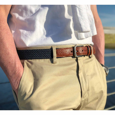 A person wearing a white shirt, khaki pants, and a Torino Italian Woven Cotton Elastic Belt Big & Tall by Torino stands outdoors near a railing with hands in pockets.