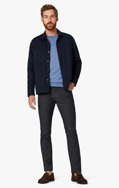 A man stands against a white background wearing 34 Heritage Black Coolmax pants, a navy jacket over a light blue shirt, and brown loafers.