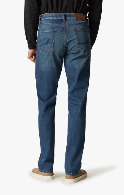 A person is shown from the back against a white background, wearing 34 Heritage Mid Cashmere straight-leg jeans by 34 Heritage, paired with a dark long-sleeve shirt and tan shoes.