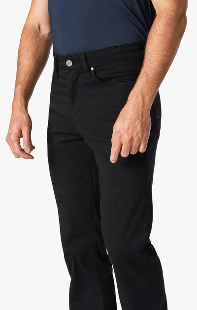 A man wears a navy shirt and 34 Heritage Double Black pants, with one hand relaxed by his side, shown from chest to thigh against a white background.
