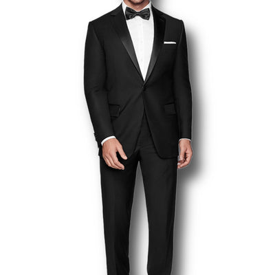 A man models the Paul Betenly Tuxedos by Paul Betenly, featuring a black modern fit tuxedo, white dress shirt, black bow tie, and pocket square against a white background, highlighting timeless men's formalwear.