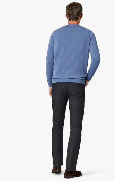 A man stands with his back to the camera, wearing a light blue sweater and 34 Heritage Black Coolmax temperature-regulating pants in dark gray, paired with brown shoes, against a plain white background.