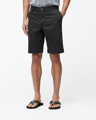 A person wearing Tommy Bahama Boracay Shorts Big & Tall in black TENCEL™ blend, a patterned shirt tucked in, and black sandals, standing against a plain white background.