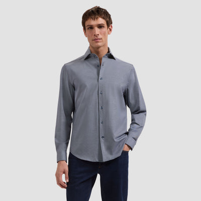 Man wearing a gray button-up shirt and dark pants on a light gray background