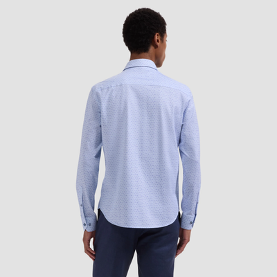 Man wearing a light blue patterned shirt and dark pants on a gray background