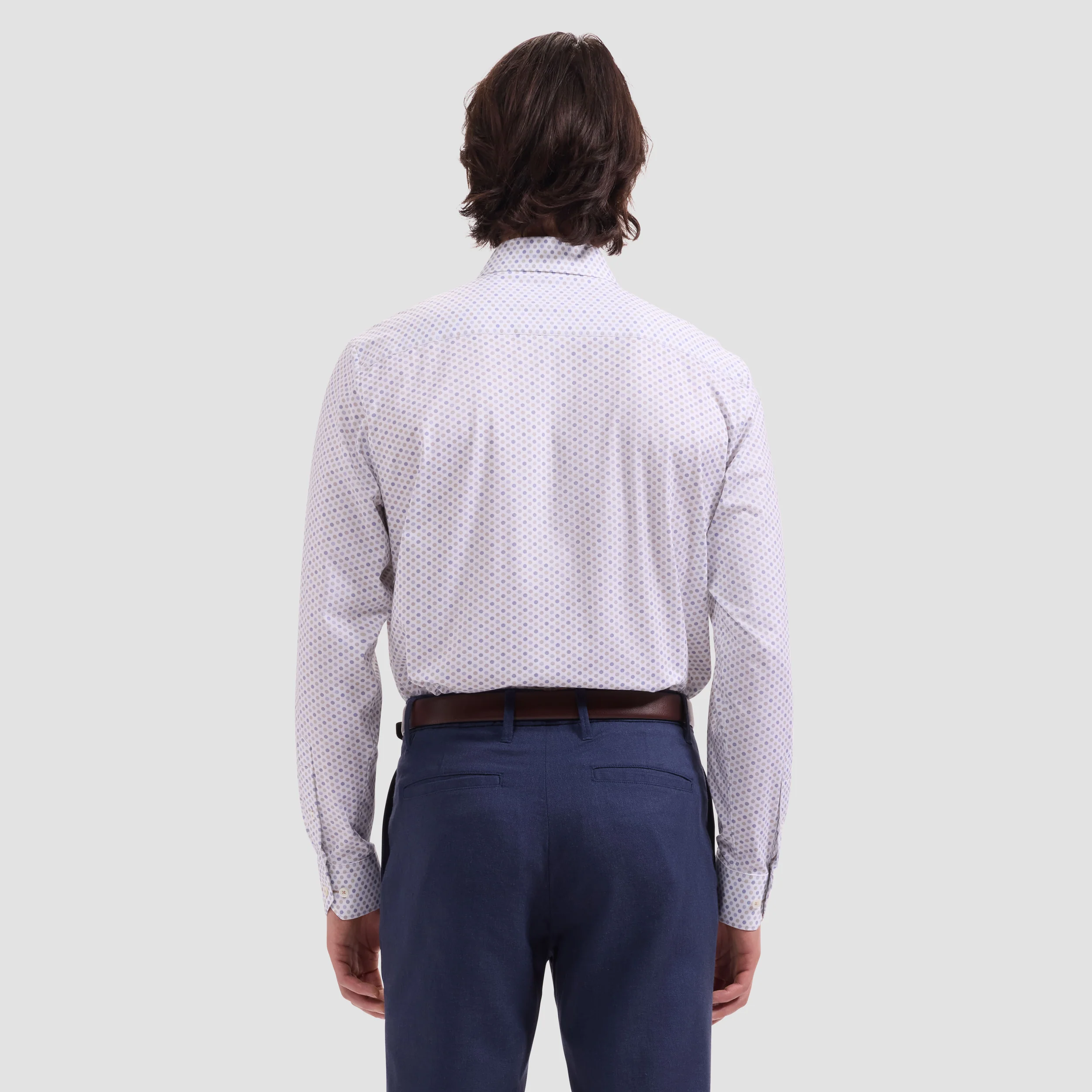 Person wearing a patterned white shirt and dark pants on a light gray background