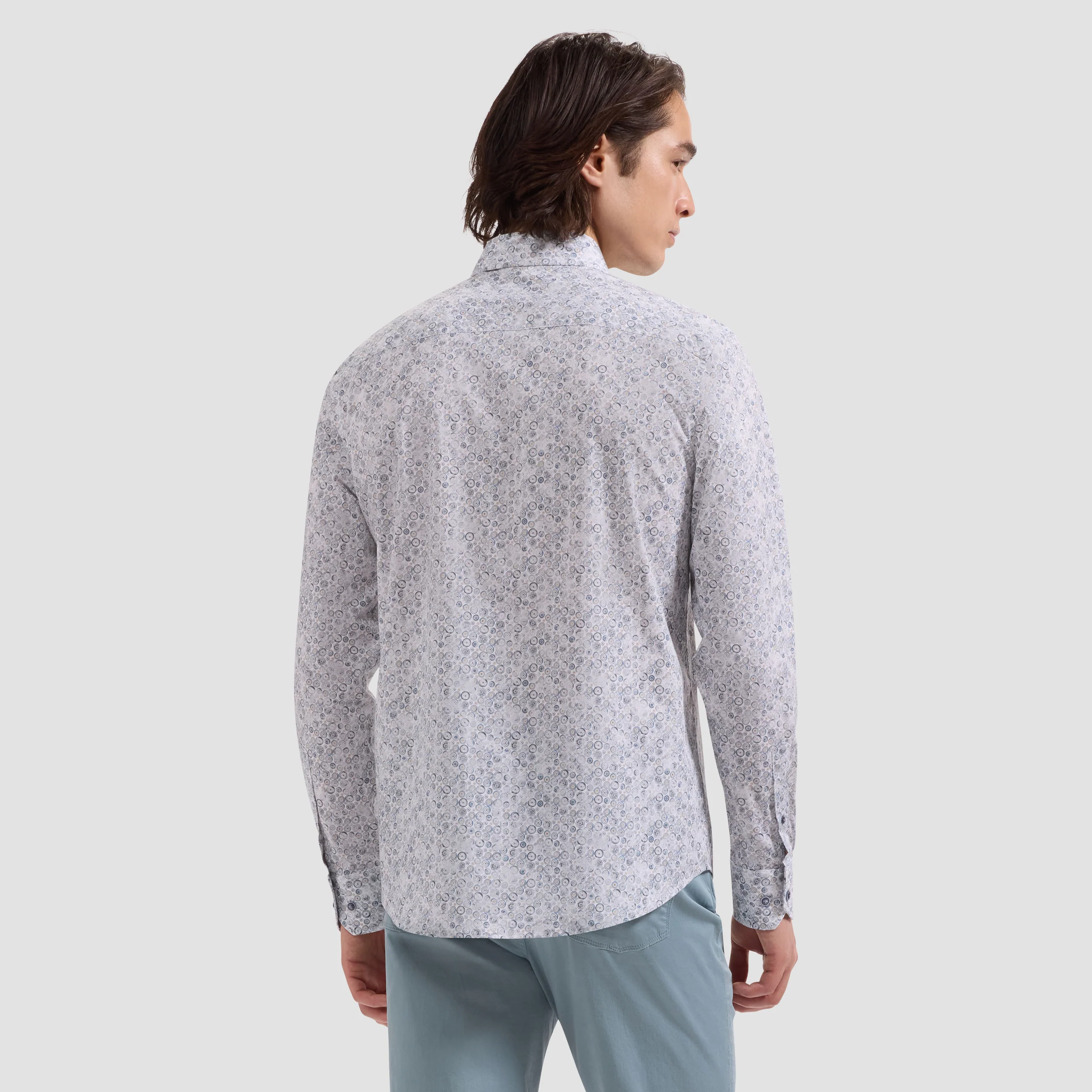 Man wearing a light gray patterned shirt and light blue pants on a white background