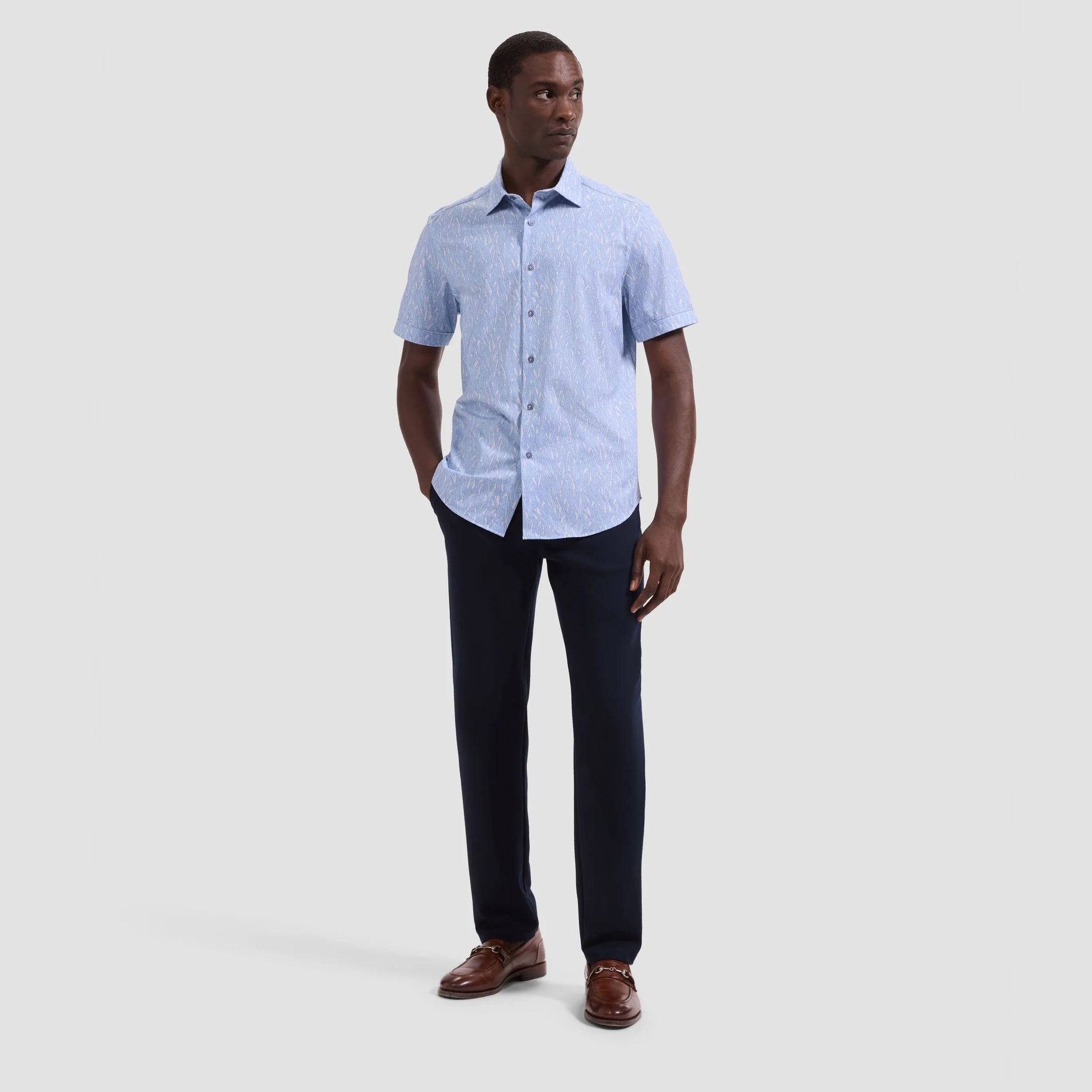 Man wearing a light blue checkered shirt and dark pants on a white background