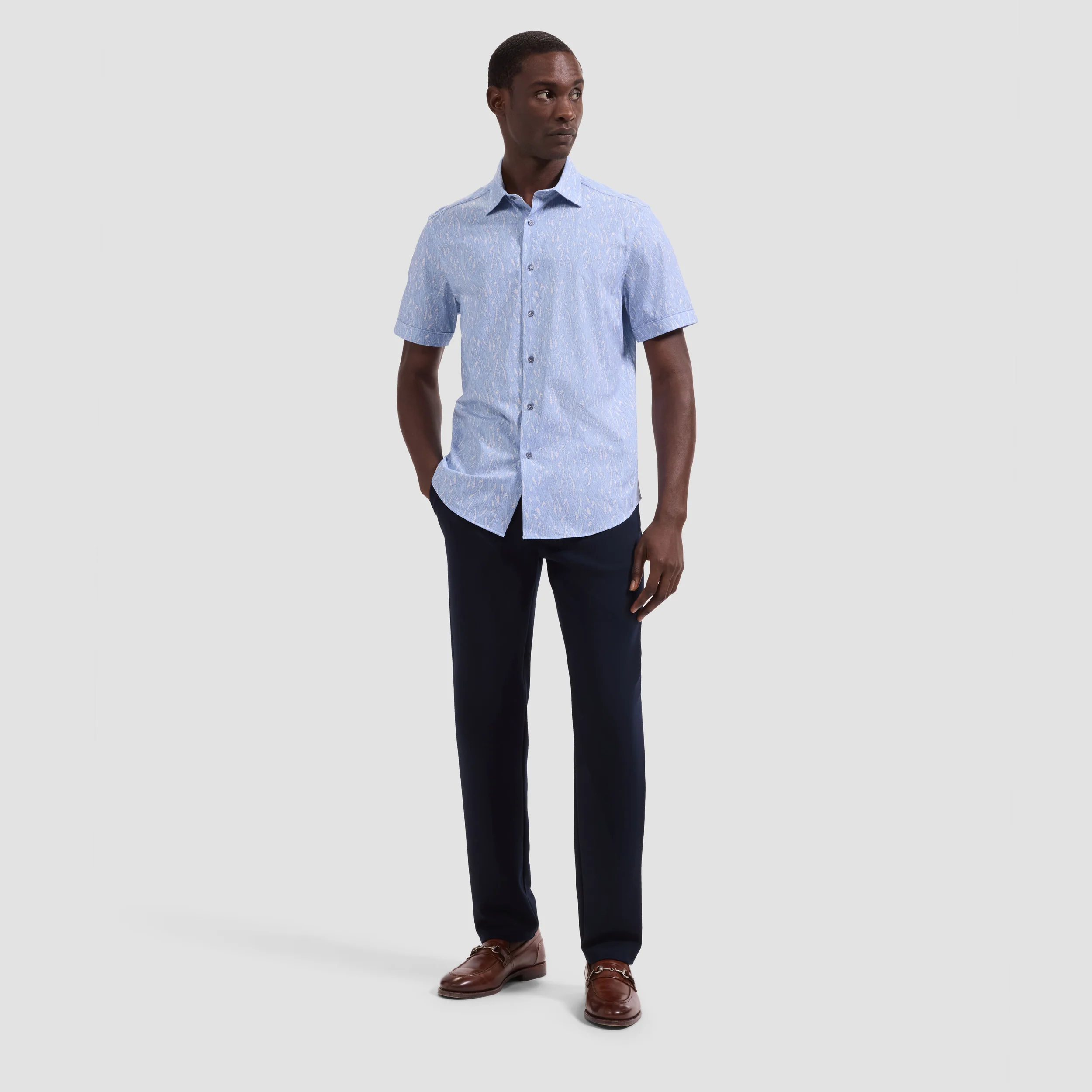 Man wearing a light blue checkered shirt and dark pants on a white background