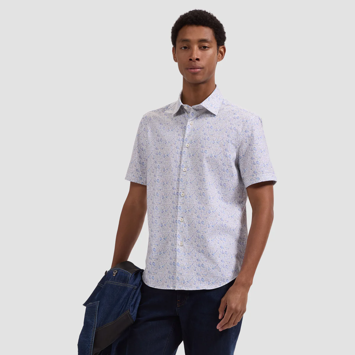 Man wearing a patterned short-sleeve shirt and dark pants against a plain background