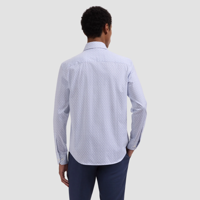Man wearing a light blue patterned shirt and dark pants on a plain background