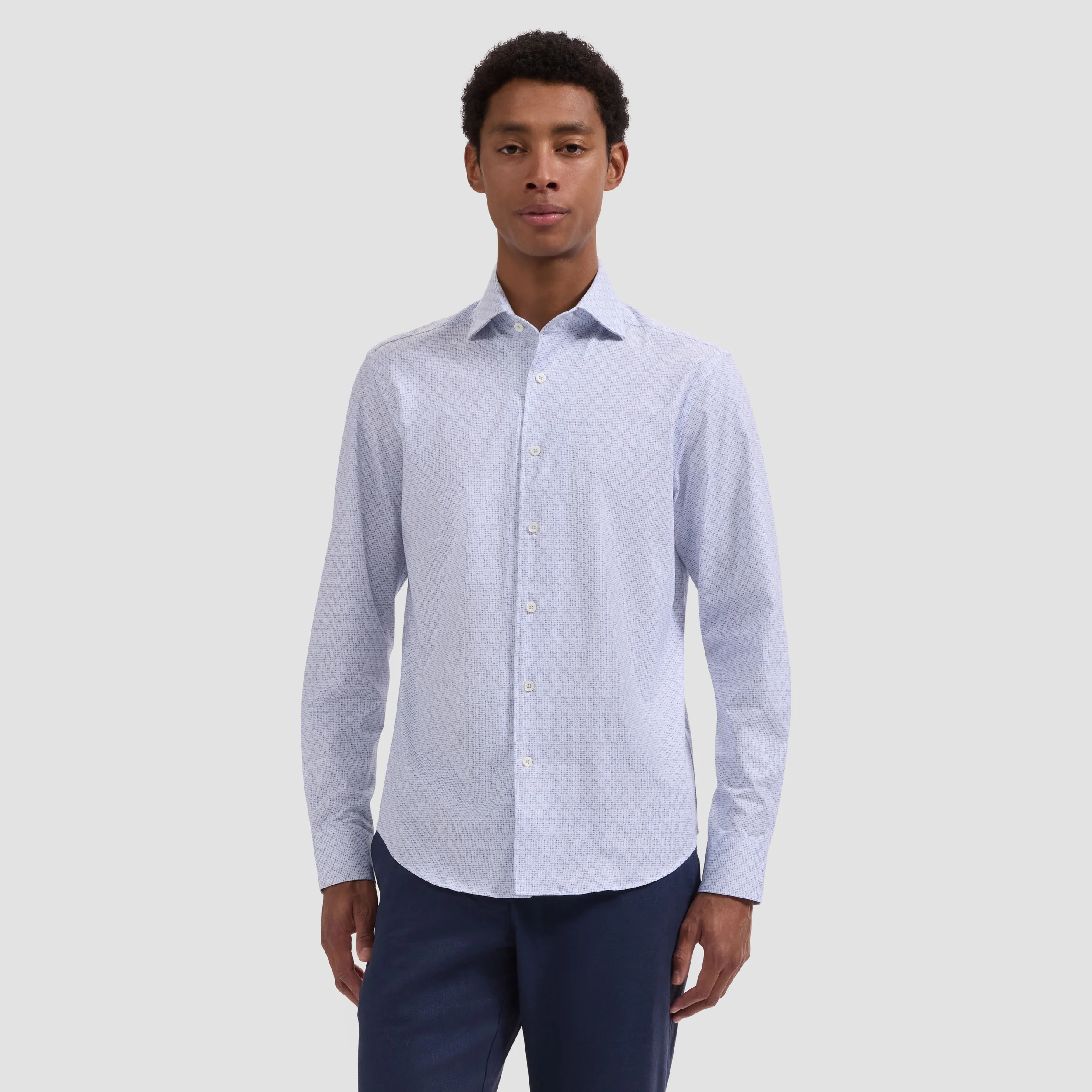 Man wearing a light blue patterned shirt and dark pants on a white background