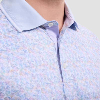 Close-up of a person in the Bugatchi S/S Three Button Performance Polo JF3600F29, featuring a pastel floral pattern, light blue collar and placket, and moisture-wicking fabric for all-day comfort.