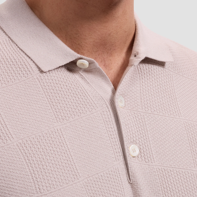Close-up of a light pink textured polo shirt with buttons on a neutral background