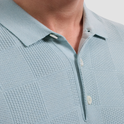 Light blue textured polo shirt with collar and buttons on a neutral background